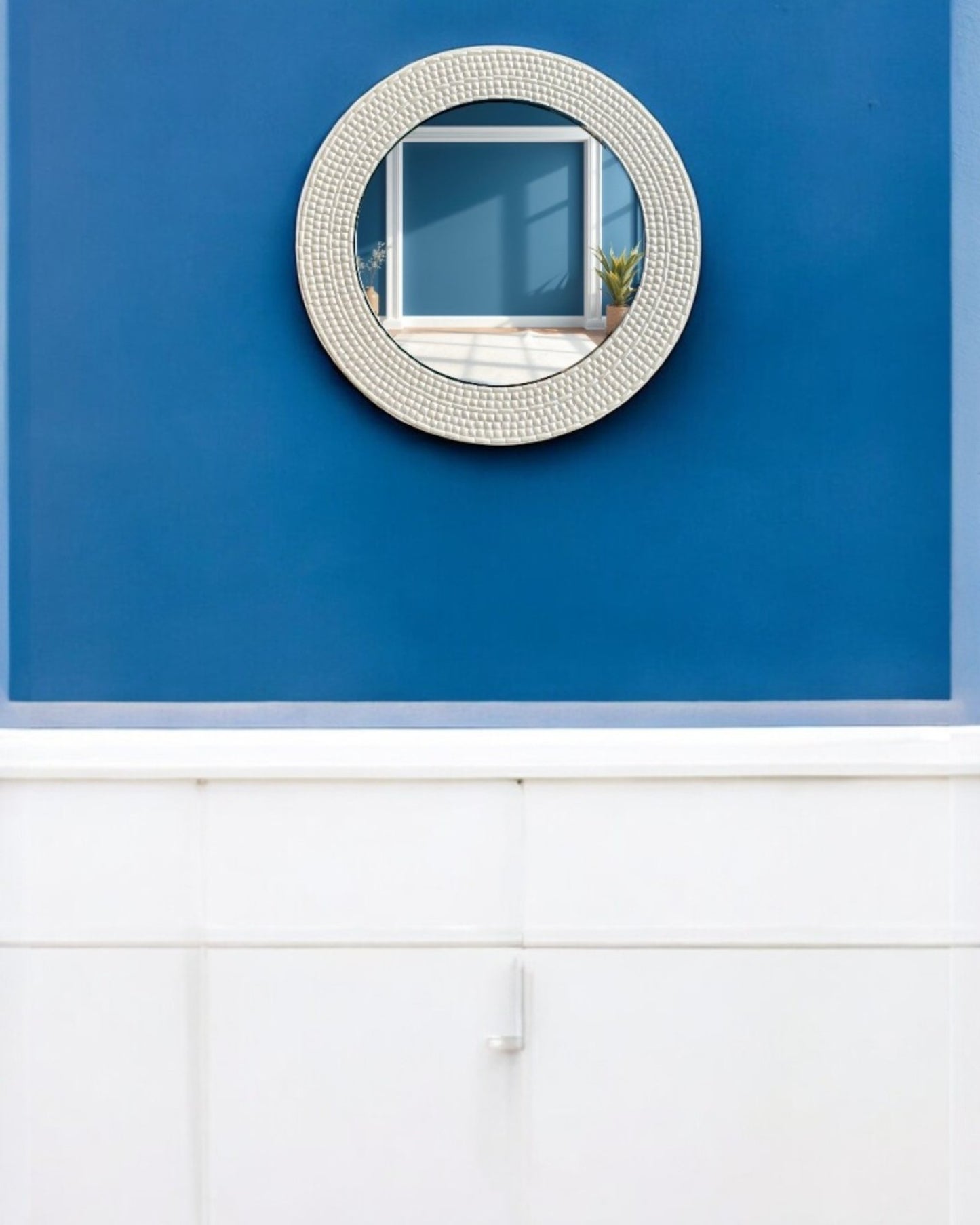 Mirroza Ivory handcrafted round mosaic mirror hanging on a blue wall
