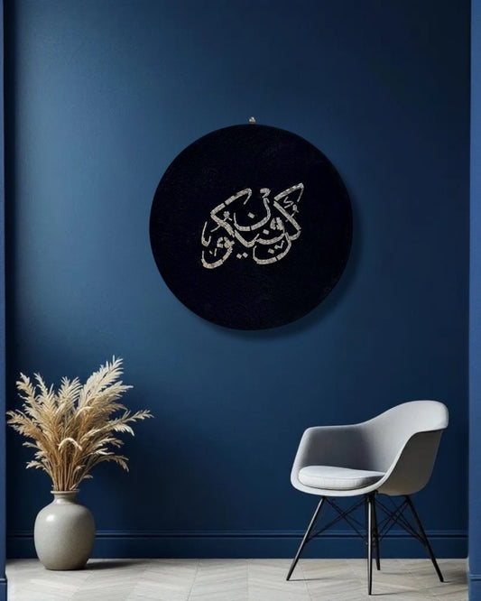 Mirroza round mirror mosaic wall art with Arabic calligraphy on a dark background, placed above a chair and plant against a blue wall.