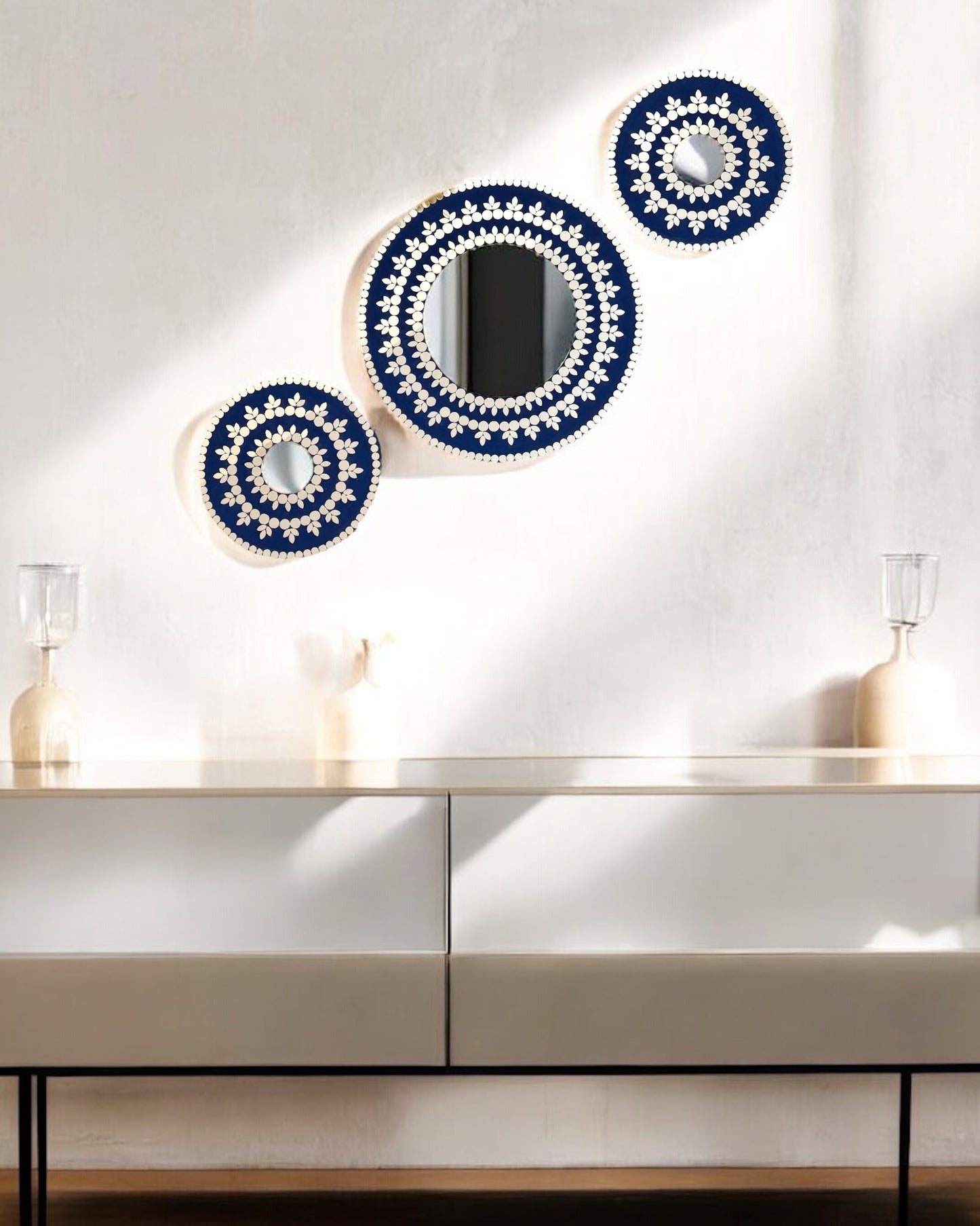Three mirror mosaic decorative mirrors with blue and white patterns on a white wall above a white cabinet.