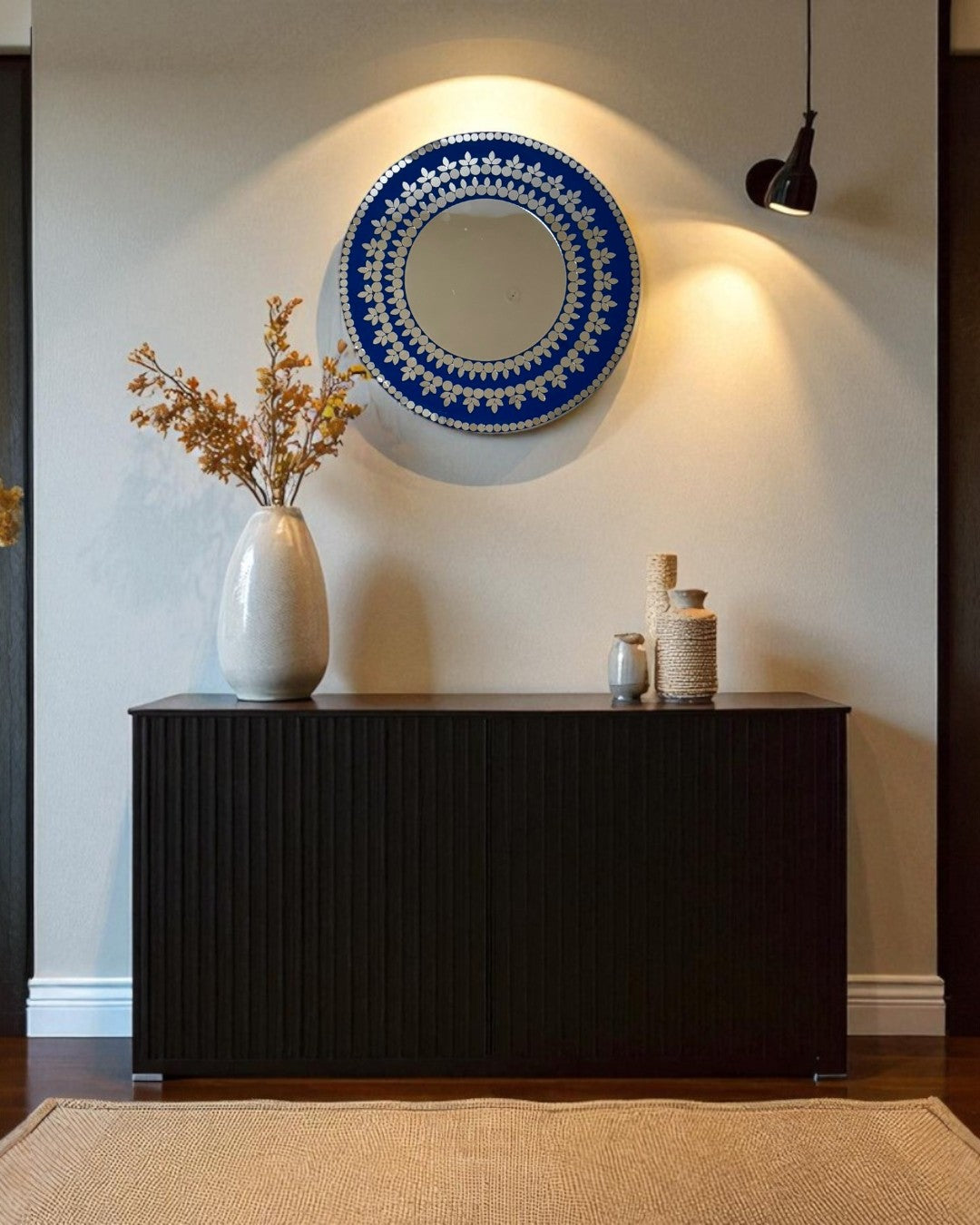 Round mosaic mirror by Mirroza styled above a console table on a dark accent hallway wall