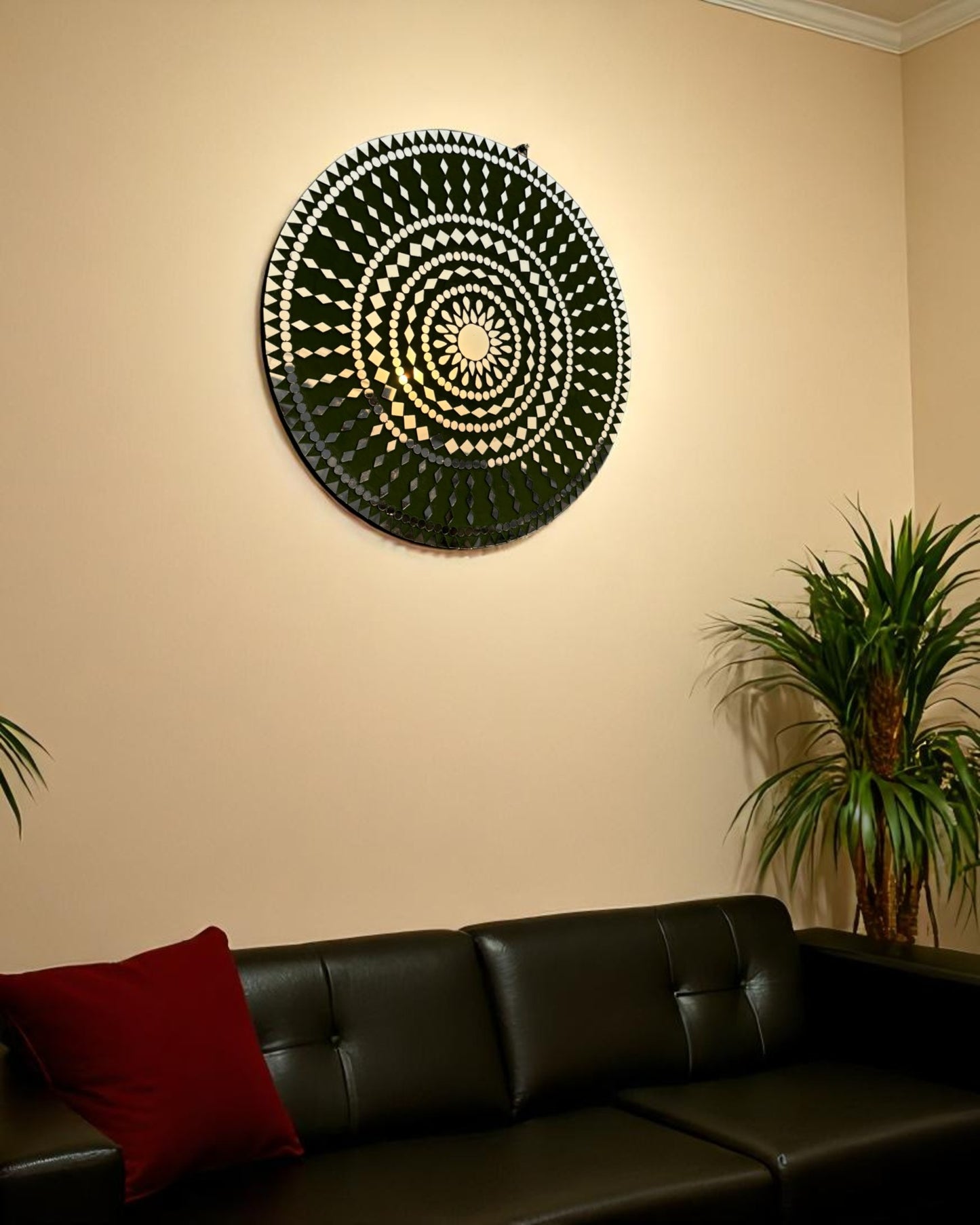 Right angle view of handcrafted Olive Bloom round mosaic wall mirror reflecting light on its intricate glass inlay on a beige wall with black sofa