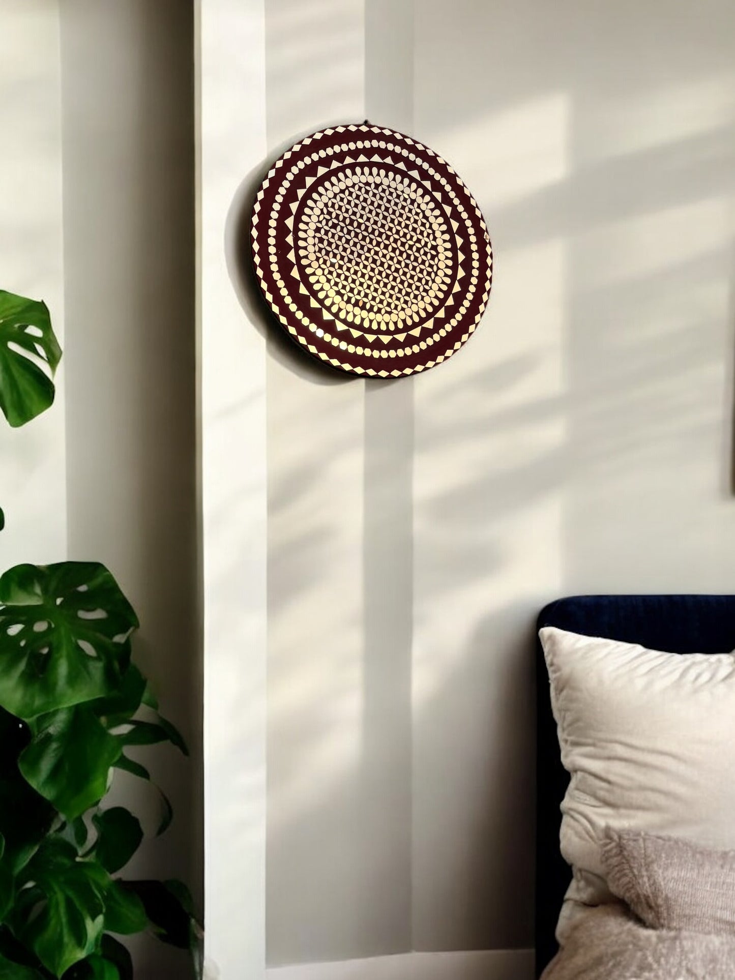 Handmade raspberry mandala mosaic wall art mirror by Mirroza hanging above a sofa in natural sunlight.