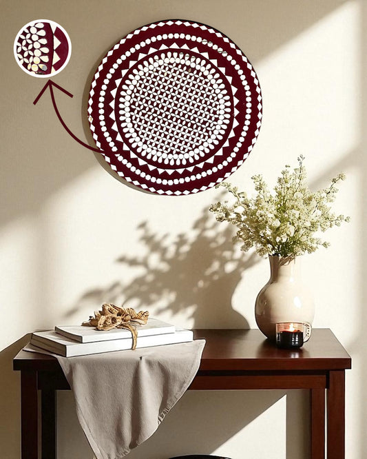 Mirroza raspberry mandala mirror mosaic decorative wall art with geometric pattern on a beige wall above a wooden table with a vase and books.