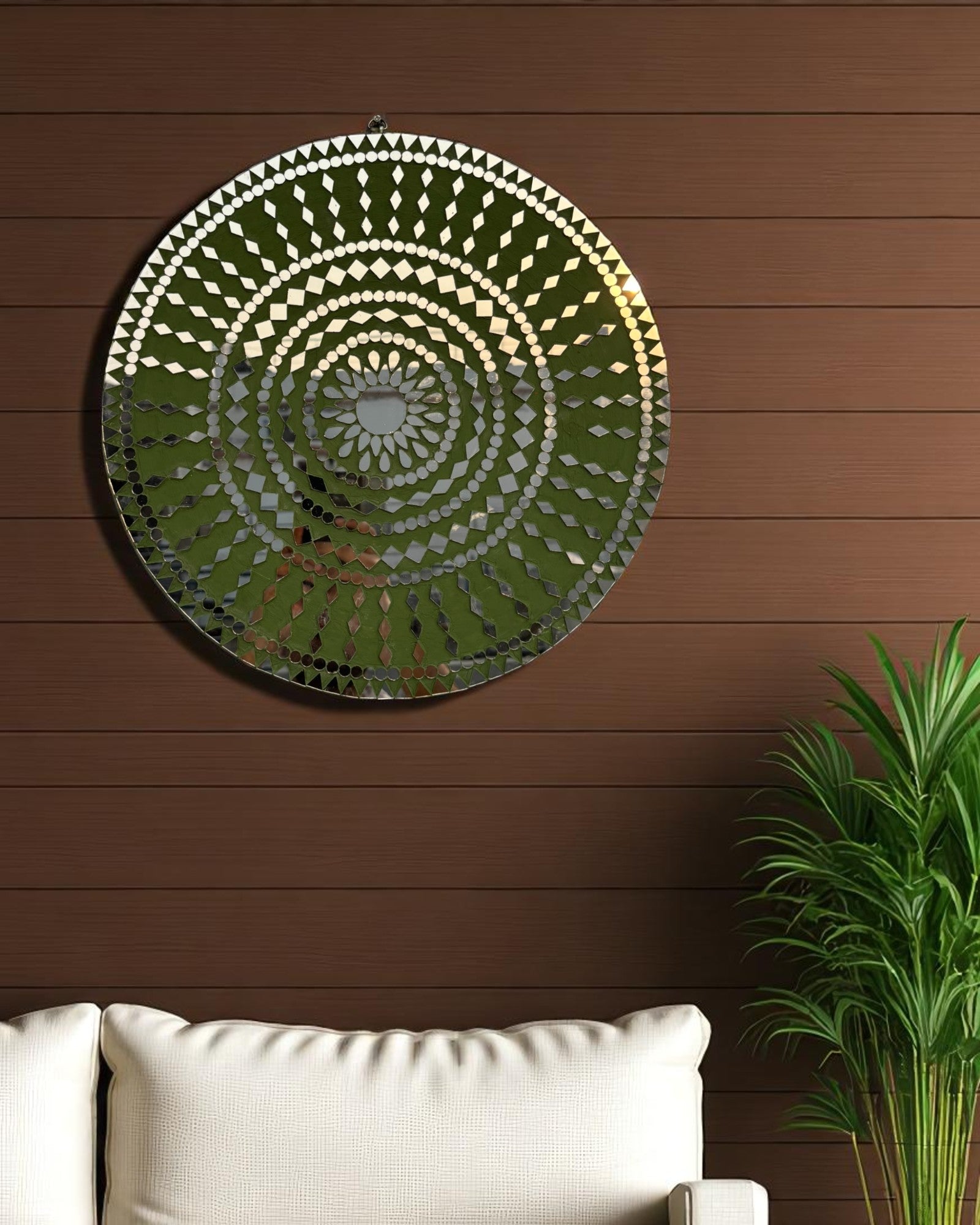Close up angle view of handcrafted Olive Bloom round mosaic wall mirror reflecting light on its intricate glass inlay on a dark wooden wall with white sofa